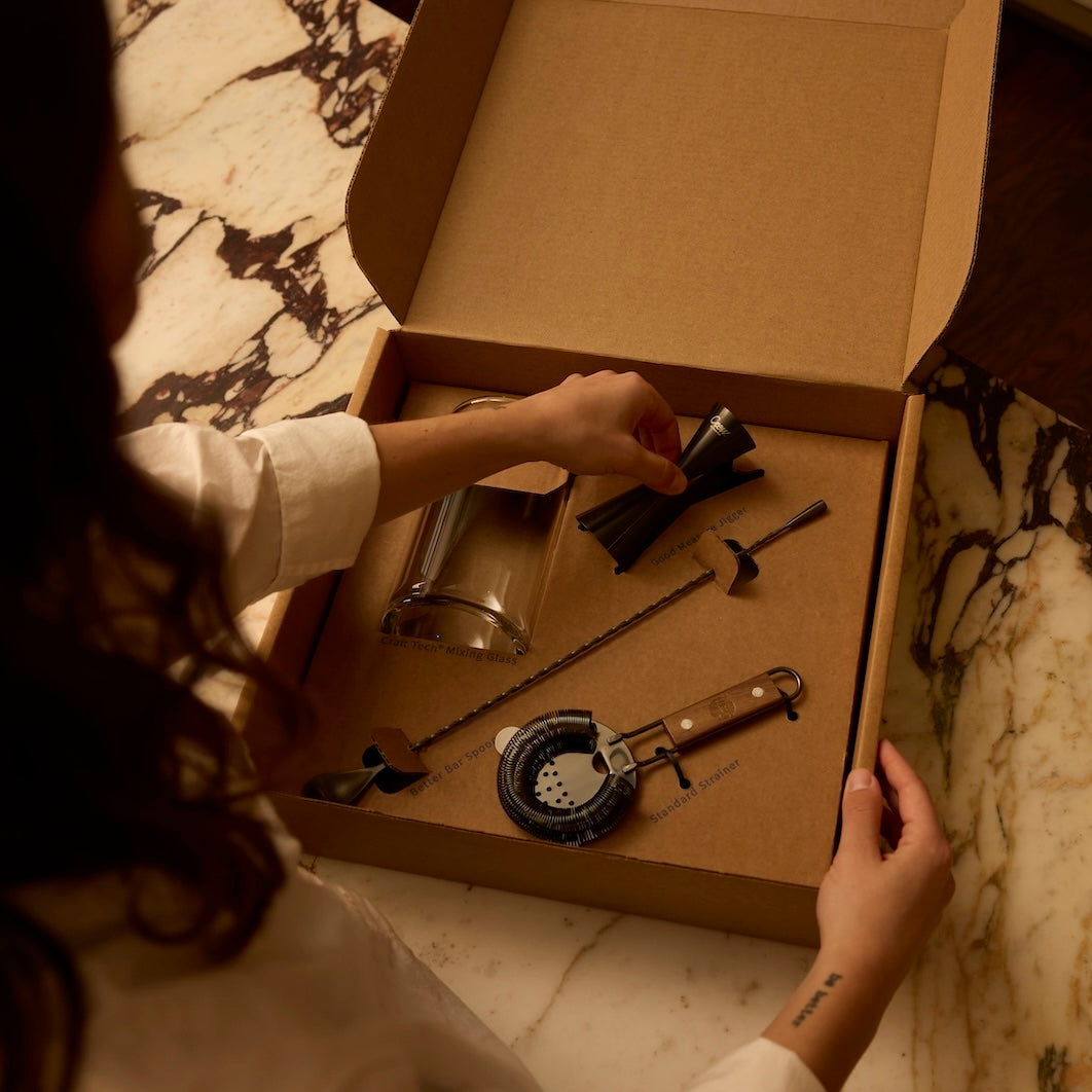 Woman placing Crew's good measure jigger as part of a bar tool set. Crew's bar tool sets and cocktail kits make great gifts for coworkers.